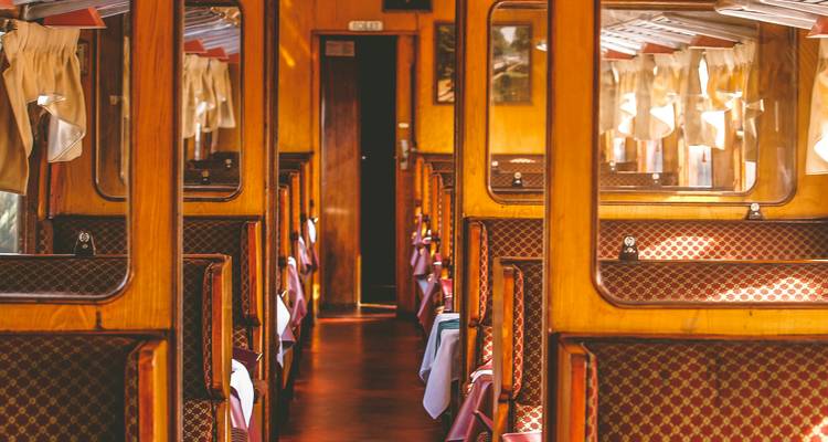 Wood-panelled corridor of a heritage dining train set with white-clothed tables and lamps.