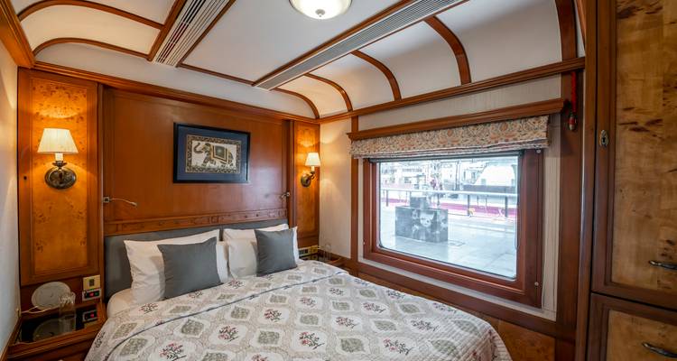 Elegant private train cabin with double bed, patterned quilt and a large window overlooking the platform.