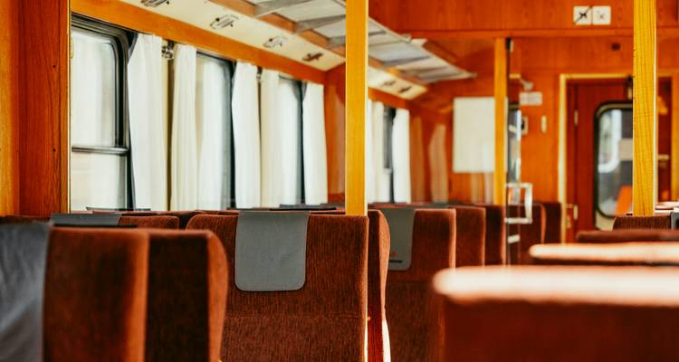 Row of brown upholstered seats inside a classic wood-trimmed railway carriage.