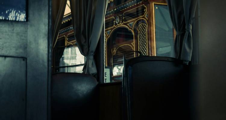Dimly lit vintage train compartment with dark leather seats and ornate wooden panelling.