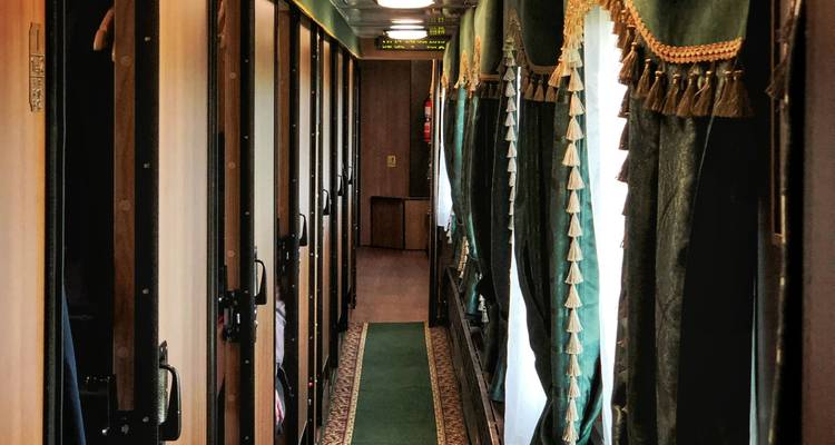 Ornate corridor of luxury train lined with green drapes and carpet runner leading to suites.