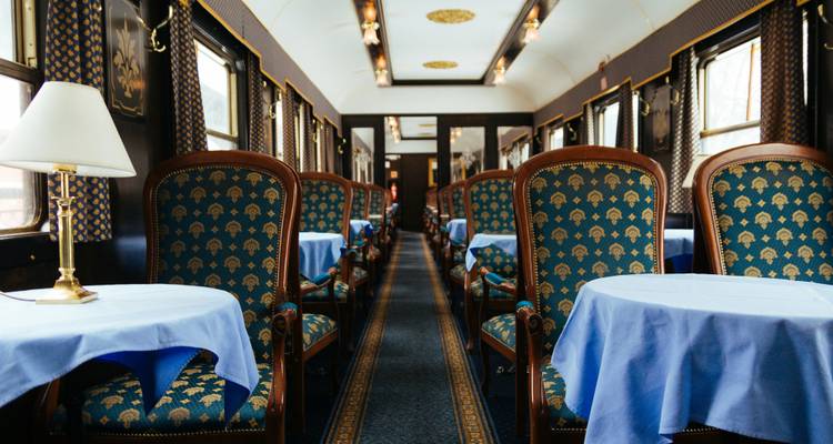 Elegant lounge car with patterned teal chairs and blue tablecloths under classic lamps.
