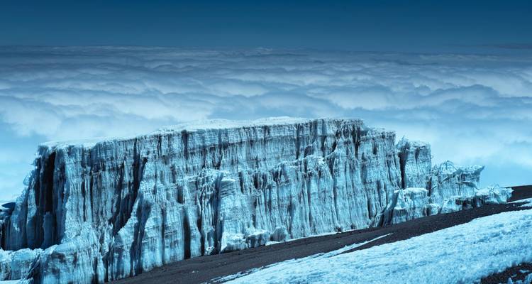 Een helderblauwe gletsjerwand rijst uit boven een zeezicht van wolken dicht bij de top van de Kilimanjaro.