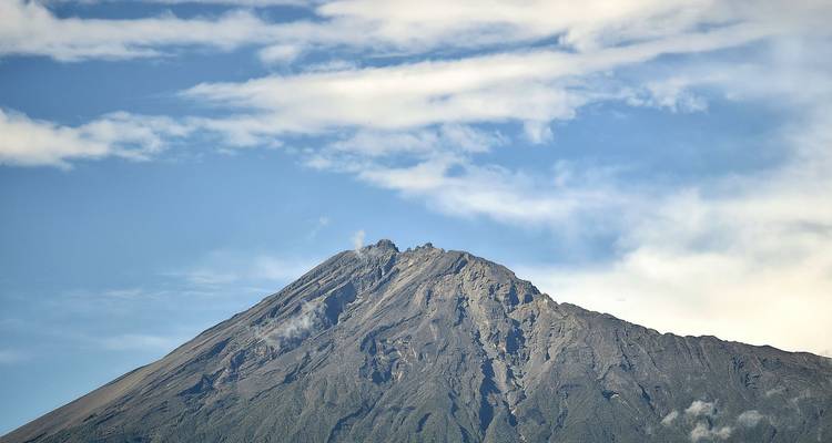 Close-up van de rotsachtige top van de Mount Meru onder gestreepte wolken tegen een blauwe lucht.