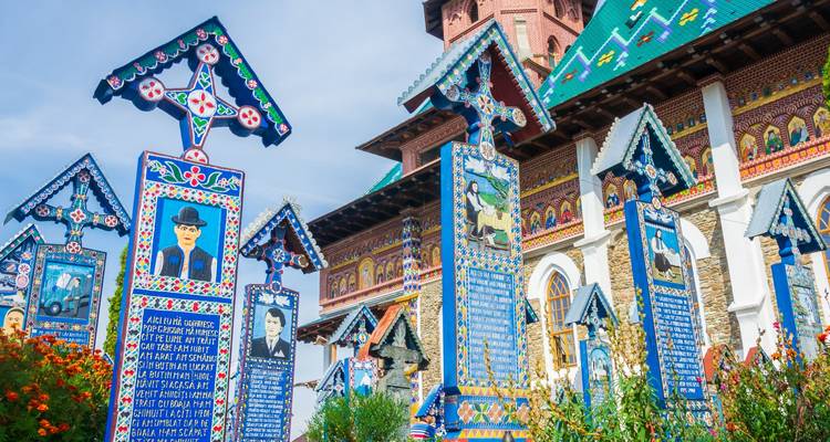 Vivid painted wooden crosses of the Merry Cemetery stand against a blue-sky backdrop.