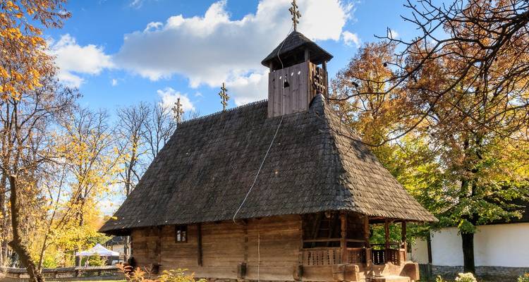 Traditional wooden church enveloped by autumn foliage under a bright sky.