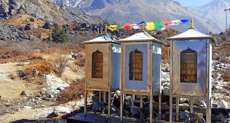 Trois moulins à prières métalliques sur des plates-formes avec des drapeaux de prière colorés dans une vallée himalayenne.