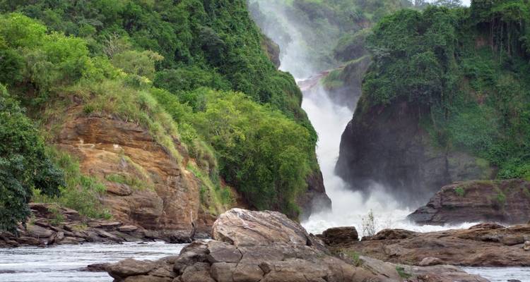 Powerful white torrents of Murchison Falls crash through a narrow gorge surrounded by lush green cliffs and rocks.