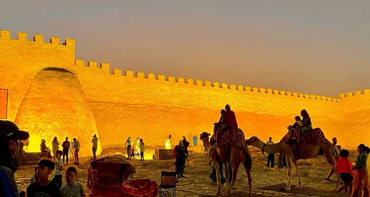 Les festivités en soirée avec des gens et des chameaux à côté des remparts en adobe brillamment illuminés baignés dans une lumière dorée.