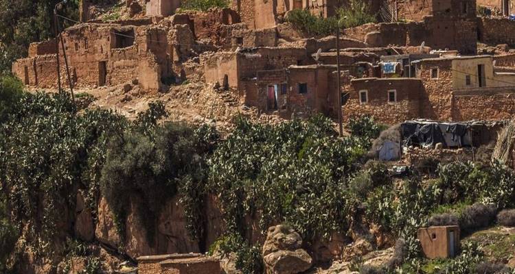 Des maisons en pierre en ruines perchées sur une falaise couverte de cactus dans une vallée accidentée.