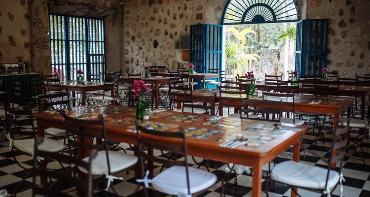 Rustic dining hall with wooden tables, checkered floor and stone walls set for a meal