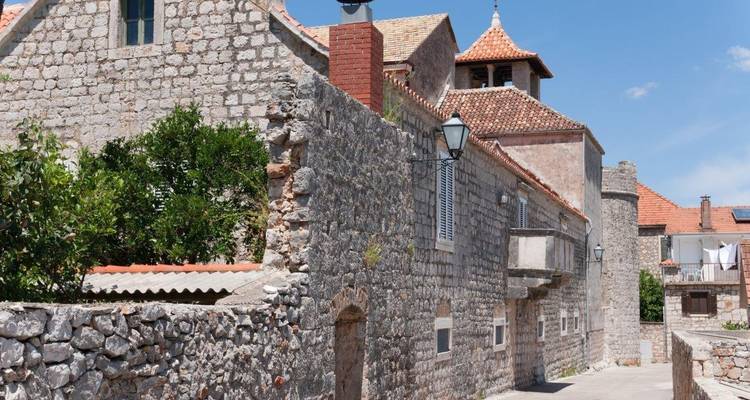 Stone alley with rustic houses and tiled roofs in a Croatian coastal village under blue sky