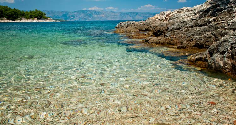 Crystal-clear shallow Adriatic water by rocky shoreline with distant islands