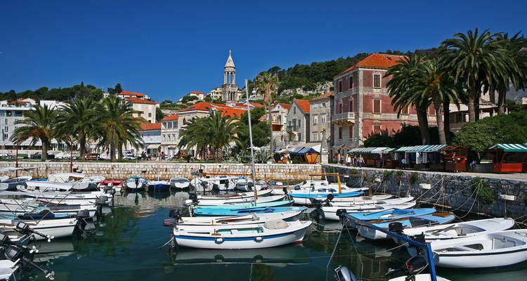 Kleine jachthaven met witte boten, palmbomen en de stenen stad Hvar onder een heldere hemel
