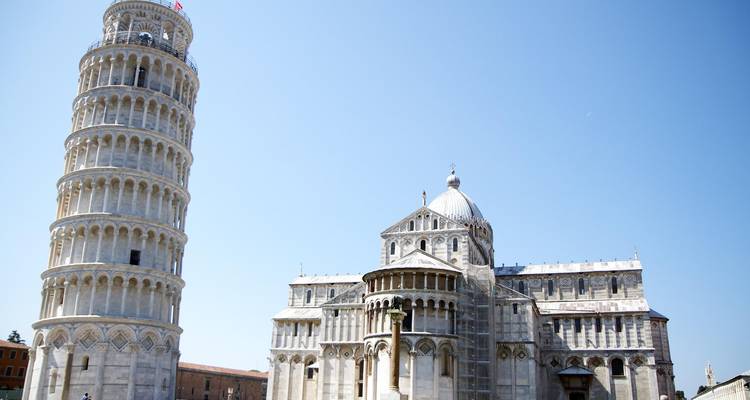 La Torre Inclinada de Pisa y el complejo de la catedral bajo un cielo azul despejado con visitantes dispersos alrededor de la base.