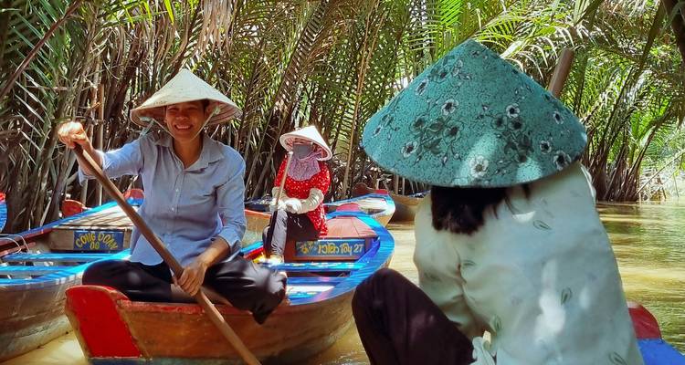 Roeiers met puntige hoeden peddelen met houten sampans door dichte nipa-palmen kanalen in de Mekongdelta.