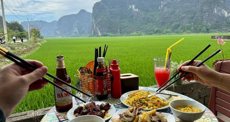 A table of Vietnamese dishes is enjoyed alfresco beside vivid green rice fields and limestone cliffs.