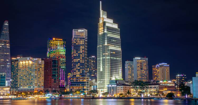 Brightly lit modern skyscrapers line the riverfront of Ho Chi Minh City after dark