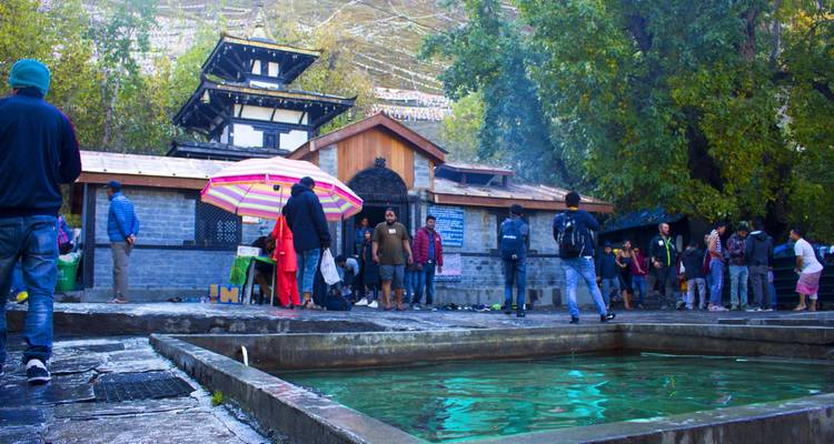 Pilgrims gather beside a rectangular holy pool in front of Muktinath Temple beneath colourful parasols.