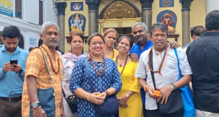 Smiling travellers wearing prayer beads pose outside an ornate temple entrance with colourful Hindu icons.