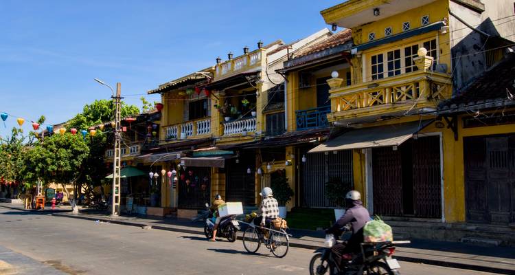 Early morning view of yellow heritage shop-houses and cyclists on a quiet Hoi An street