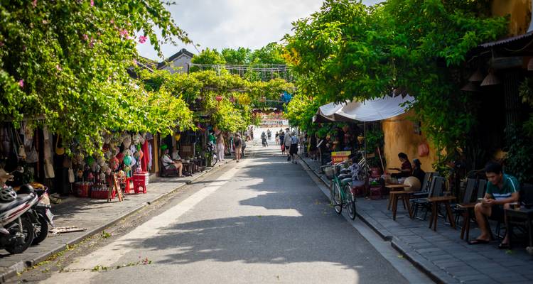 Leafy pedestrian lane in Hoi An flanked by shops and flowering trellises