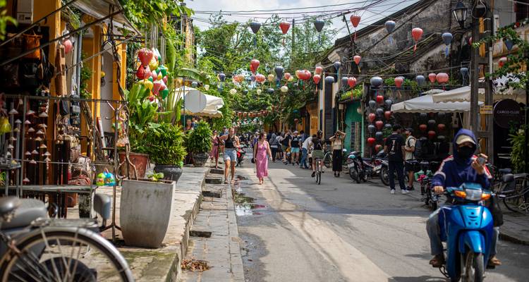 Bustling lantern-decorated street in Hoi An with tourists walking and motorbike passing