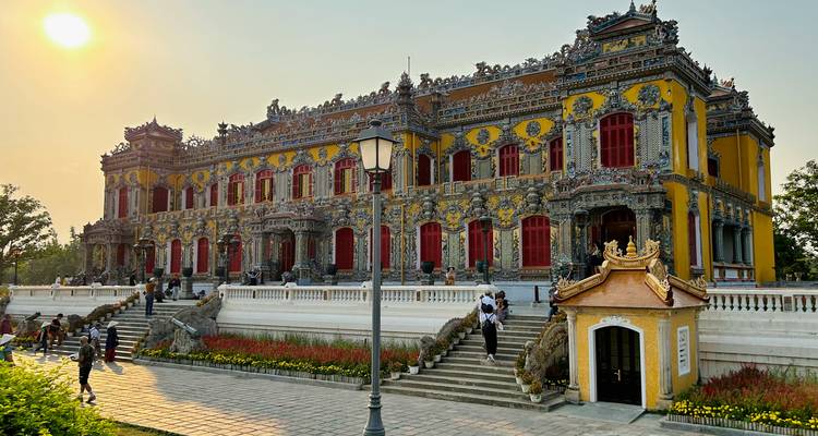 An ornate yellow royal building in Hue’s Imperial City glows in the low afternoon sun as visitors ascend its steps.
