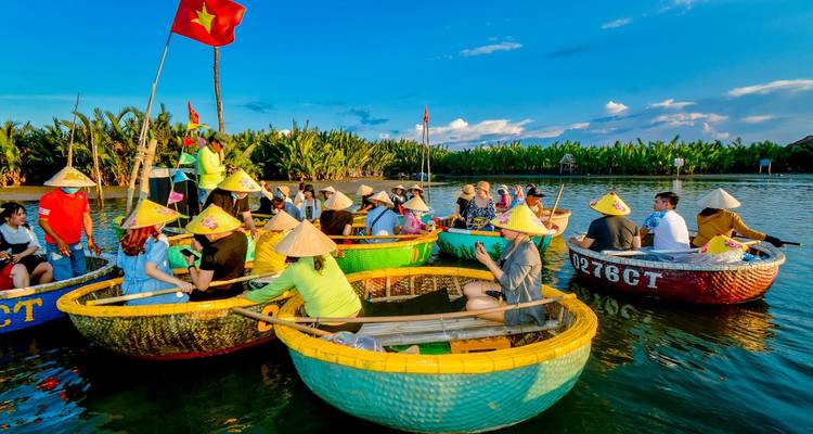 Clusters of tourists sit in round bamboo basket boats on a calm river surrounded by green palms near Hoi An.