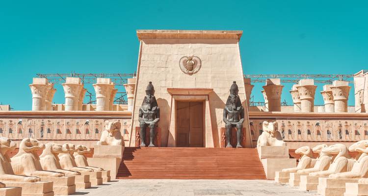 Movie-set style temple façade with colossal statues and ram sphinxes under turquoise sky