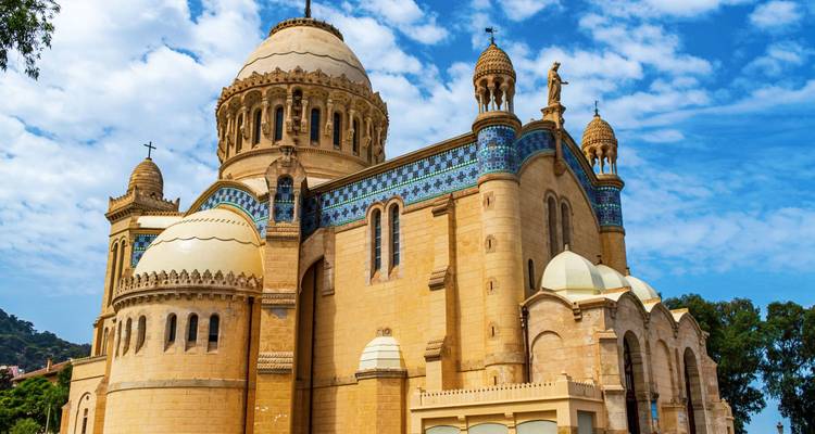 Grand stone basilica with domes and mosaics stands against a bright blue sky with scattered clouds.