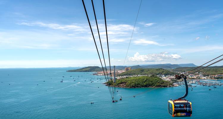 Long cable car lines stretch over turquoise sea toward a coastal town on an island