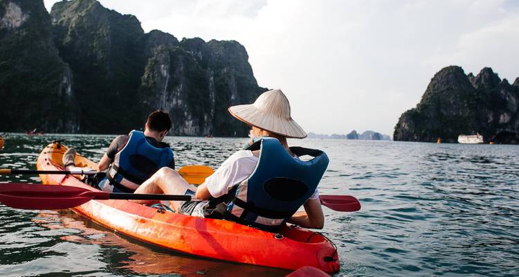Two people kayaking on turquoise water with limestone cliffs of Ha Long Bay.