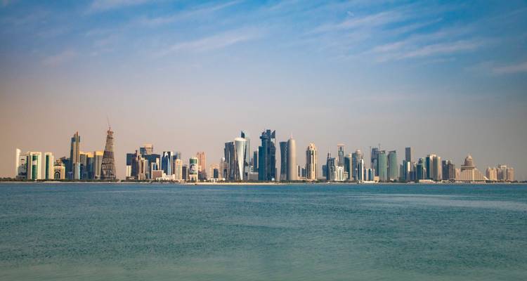 Vue panoramique de la ligne d'horizon des gratte-ciel modernes de Doha s'élevant au-dessus des eaux calmes et bleues du Golfe sous un ciel légèrement nuageux.