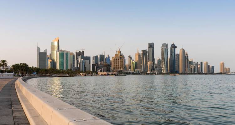 La promenade sinueuse de la Corniche de Doha longeant les eaux scintillantes avec la skyline moderne dans la douce lumière du soir.