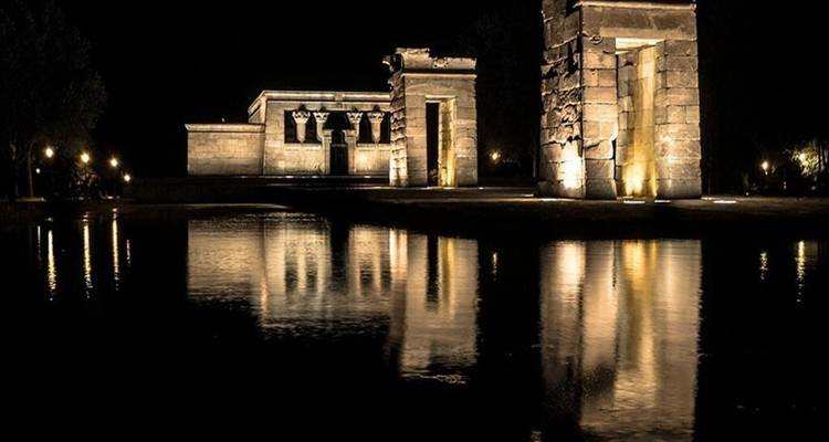 Reflet nocturne de structures de temple ancien illuminées sur une eau calme créant une image miroir.