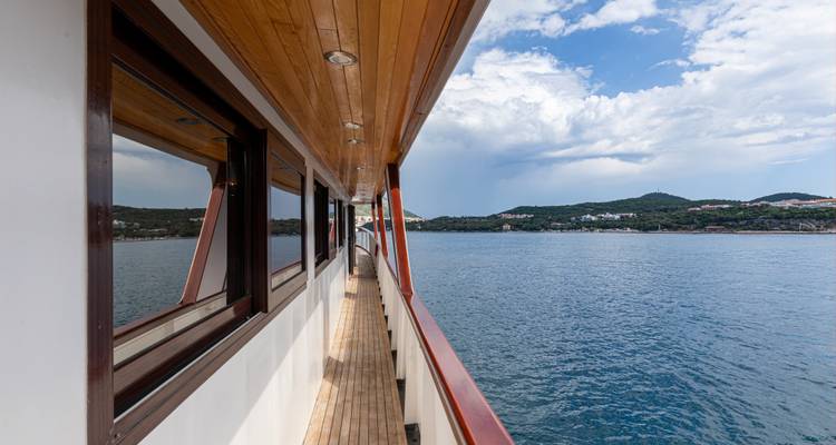 Schmal gestaltetes Holzpromenadendecke mit Meerblick entlang der Seite eines Kreuzfahrtschiffes.