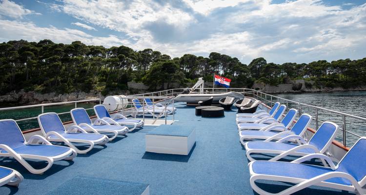 Sonnendeck mit Reihen von blauen Liegestühlen mit Blick auf eine bewaldete Insel und die kroatische Flagge.
