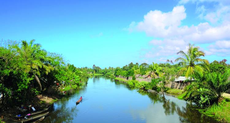 Calm tropical river flanked by lush vegetation and small thatched villages with a lone canoe.