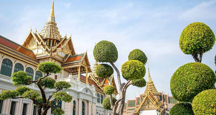 Netjes gemanicuurde topiaire bomen omlijsten de elegante daken van het Grote Paleis complex van Bangkok.