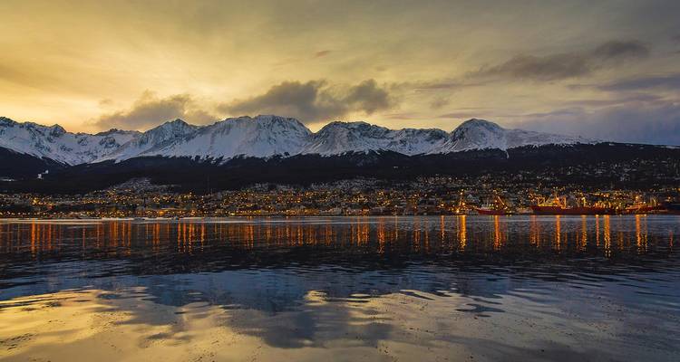 Les lumières du soir d'Ushuaia se reflètent sur les eaux calmes sous des montagnes enneigées au crépuscule.