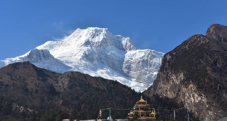 Macizo himalayo cubierto de nieve que se eleva detrás de un monasterio dorado y banderas de oración.