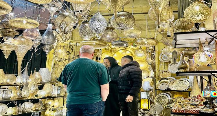 Overdekte marktstandaarde vol met sierlijke koperen lampen waar winkeliers rondkijken