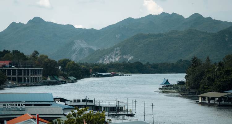 Wide river flanked by forested hills with floating houses and distant mountains