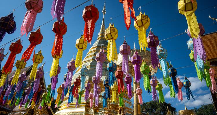 Colorful paper lanterns hanging above a gleaming golden stupa against a vivid blue sky