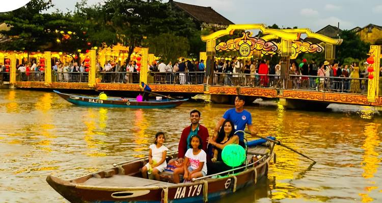 Crowds watch families riding wooden boats on a lantern-lit river near an ornate bridge in Hoi An.