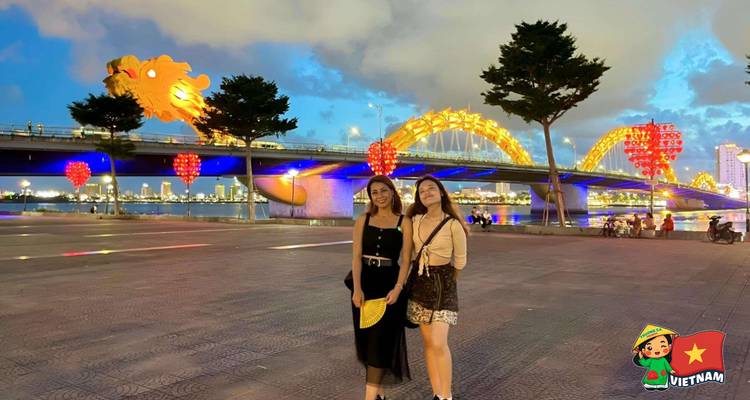 Two friends pose in front of Da Nang’s illuminated Dragon Bridge during blue hour.