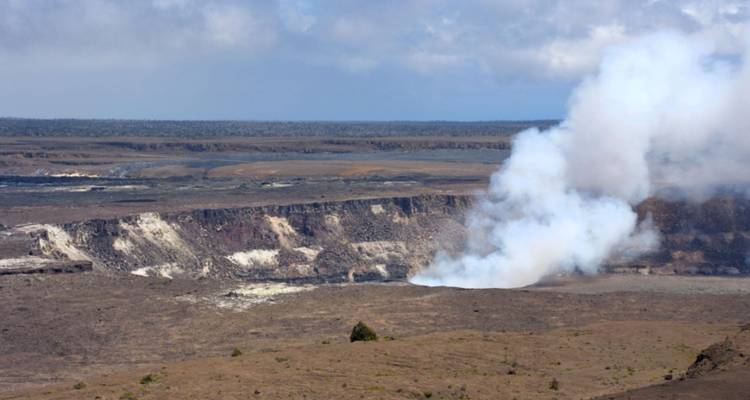 Volcanic crater emitting a plume of steam amidst a barren lava landscape.