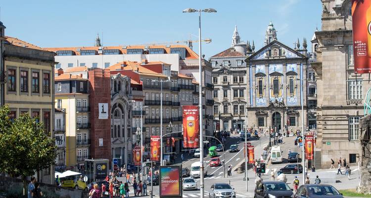 Belebte Straße in der Innenstadt von Porto mit einer mit Azulejos gefliesten Kirche, farbenfrohen Gebäuden und Menschenmengen sowie Fahrzeugen.