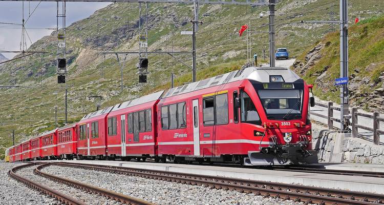 Langer Bernina Express Zug, der sich entlang von Bergbahnlinien in einer felsigen Alpenlandschaft schlängelt.